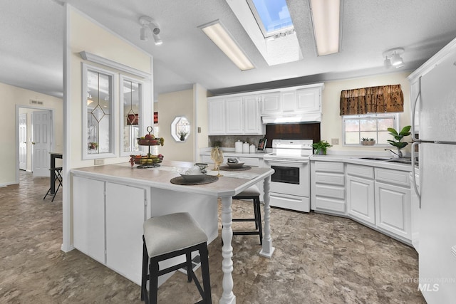 kitchen featuring under cabinet range hood, light countertops, white appliances, a skylight, and white cabinetry
