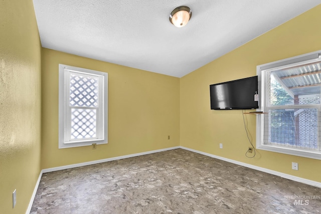 unfurnished room with lofted ceiling, baseboards, and a textured ceiling