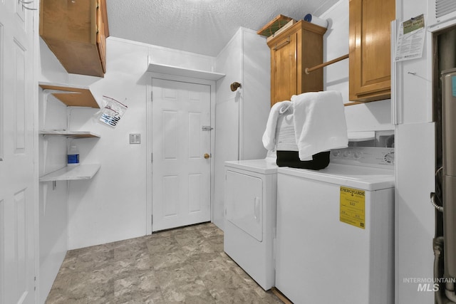 clothes washing area featuring stone finish flooring, washer and dryer, a textured ceiling, and cabinet space
