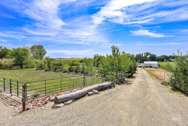 view of street with gravel driveway, a rural view, and a gated entry