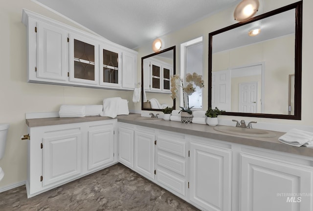 bathroom with a sink, a textured ceiling, double vanity, and toilet