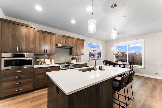 kitchen featuring a kitchen island with sink, sink, stainless steel appliances, and light hardwood / wood-style floors