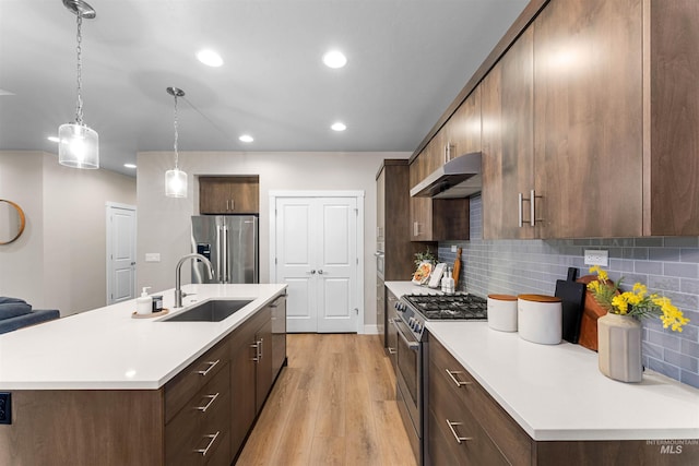 kitchen with backsplash, sink, hanging light fixtures, light wood-type flooring, and stainless steel appliances