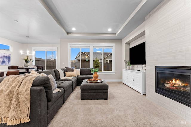 living room featuring a raised ceiling, a fireplace, light carpet, and an inviting chandelier