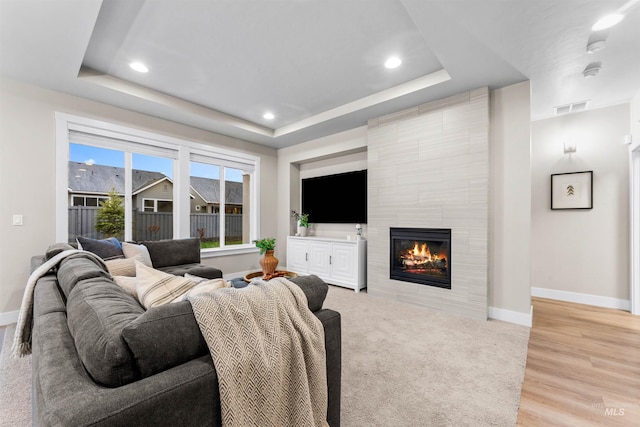 living room featuring a tray ceiling, a tiled fireplace, and light hardwood / wood-style flooring