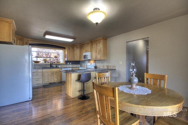 kitchen with dark wood finished floors, dark countertops, a sink, white appliances, and a peninsula