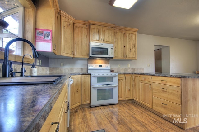 kitchen with dark countertops, white appliances, a sink, and light wood-style flooring