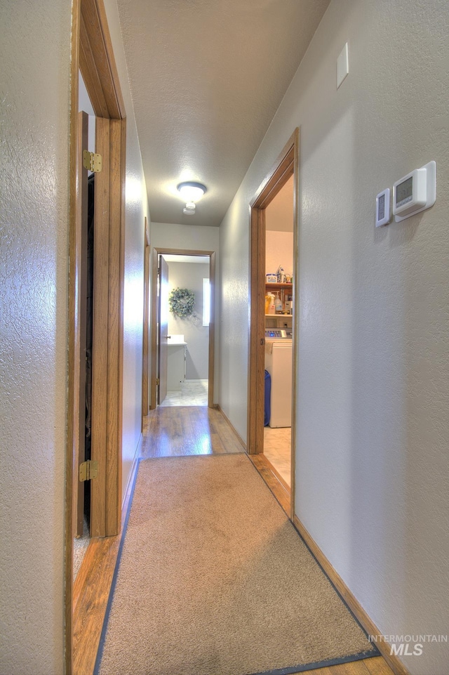 hall featuring light wood-style floors, washer / dryer, a textured wall, and baseboards
