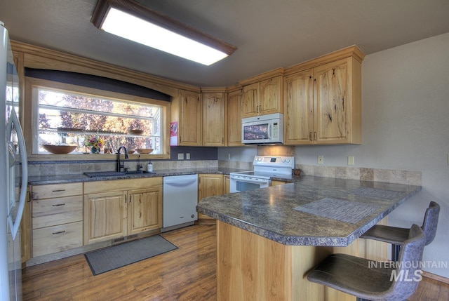 kitchen featuring white appliances, dark countertops, a peninsula, a kitchen bar, and a sink