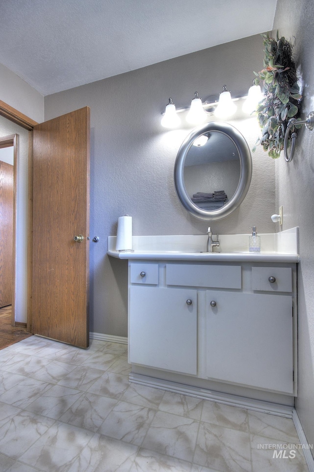 bathroom with marble finish floor, vanity, baseboards, and a textured ceiling