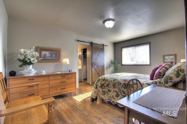 bedroom with light wood-style floors, a textured ceiling, and a barn door