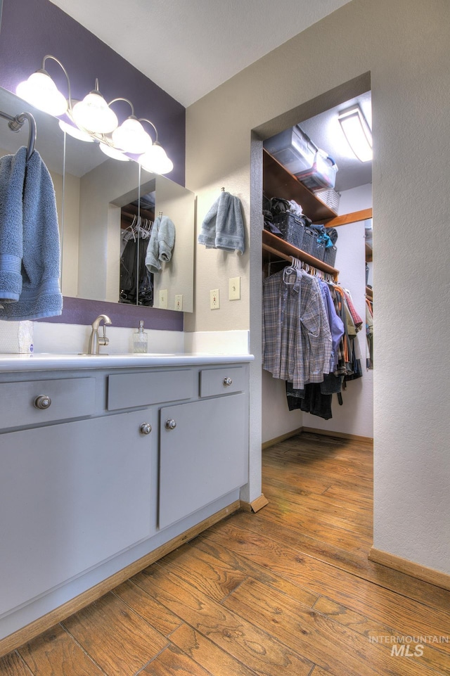 bathroom featuring baseboards, a spacious closet, vanity, and wood finished floors