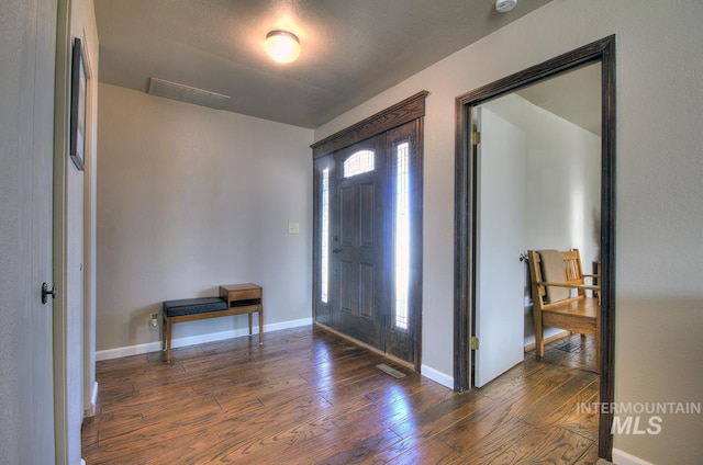 foyer with dark wood-style flooring, visible vents, and baseboards