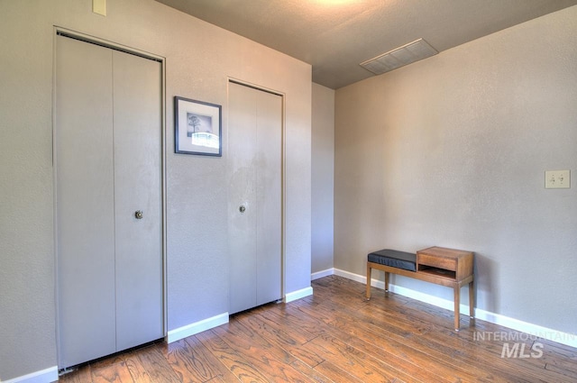 unfurnished bedroom featuring two closets, baseboards, visible vents, and wood finished floors