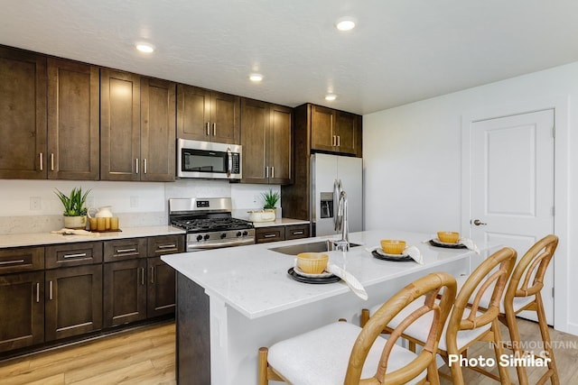 kitchen featuring a breakfast bar area, a sink, stainless steel appliances, dark brown cabinets, and light wood-style floors