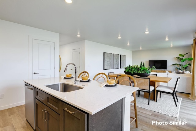 kitchen with dishwasher, a breakfast bar area, light wood-style floors, and a sink