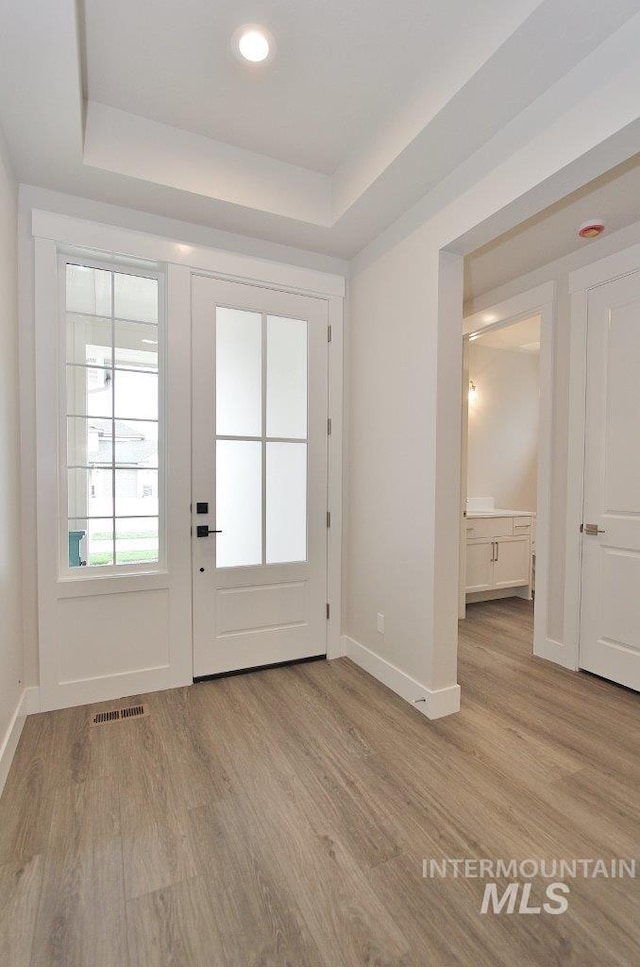 doorway to outside featuring a raised ceiling and light wood-type flooring