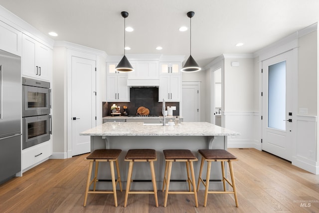 3051 S Sedgebrook Ln, Eagle, ID 83616 - kitchen with appliances with stainless steel finishes, white cabinetry, a kitchen bar, recessed lighting, and a wainscoted wall