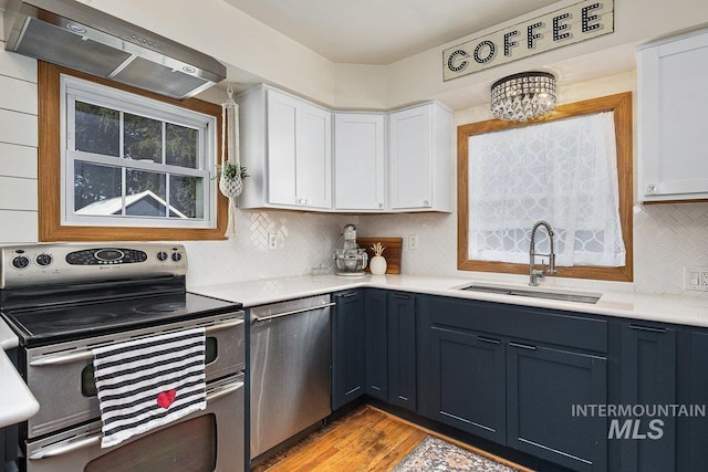 kitchen featuring a sink, white cabinetry, stainless steel appliances, wall chimney exhaust hood, and light countertops