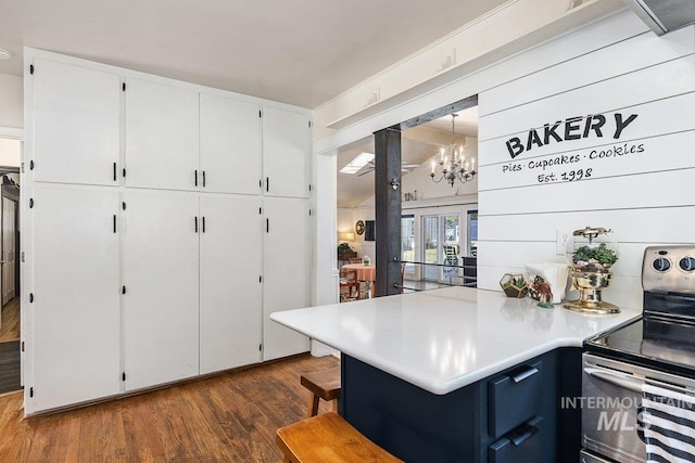 kitchen featuring light countertops, stainless steel electric range, a peninsula, white cabinets, and dark wood-style flooring