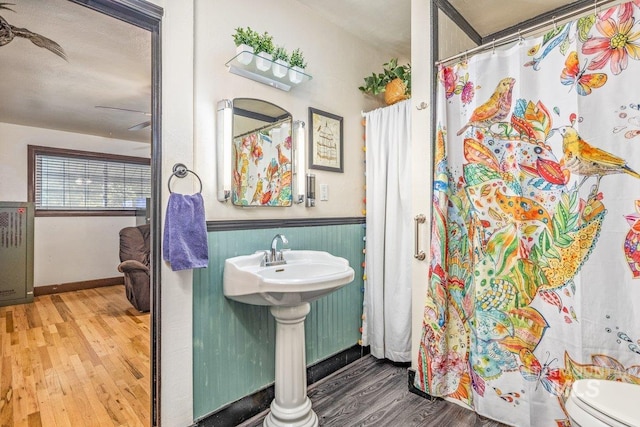 bathroom with toilet, a shower with shower curtain, wainscoting, wood finished floors, and a sink