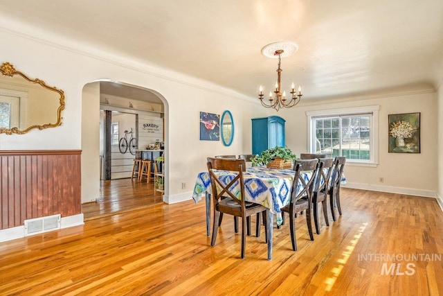 dining space with visible vents, light wood-style flooring, arched walkways, crown molding, and a chandelier