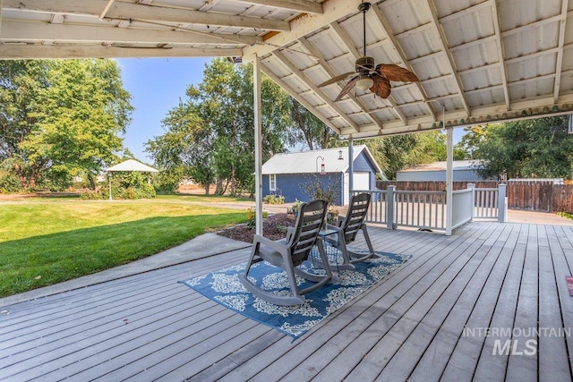 wooden deck featuring a yard, an outdoor structure, a ceiling fan, and fence