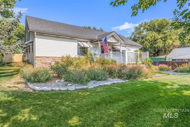 view of front facade with stone siding, roof with shingles, a front yard, and fence