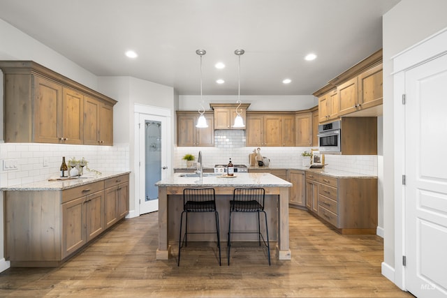10685 W Evelia St, Boise, ID 83709 - kitchen with brown cabinets, decorative backsplash, light stone countertops, an island with sink, and wood finished floors