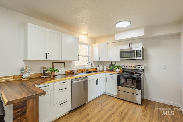 kitchen featuring butcher block countertops, sink, light wood-type flooring, appliances with stainless steel finishes, and white cabinets