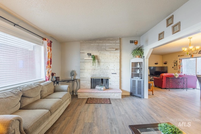 living room featuring hardwood / wood-style flooring, a large fireplace, a notable chandelier, and a textured ceiling