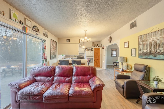 living room featuring a textured ceiling, vaulted ceiling, a chandelier, and light wood-type flooring