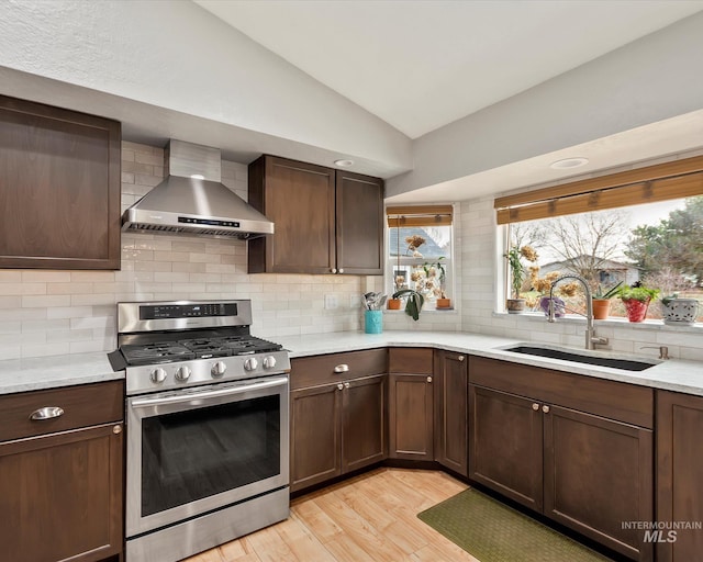 kitchen with wall chimney range hood, gas range, light countertops, vaulted ceiling, and a sink