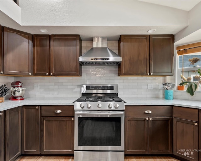 kitchen featuring backsplash, dark brown cabinetry, wall chimney range hood, stainless steel gas range, and vaulted ceiling