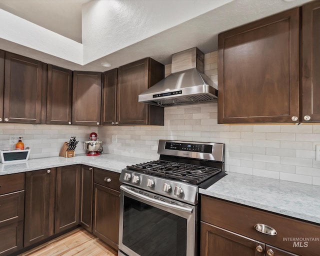 kitchen featuring light wood-type flooring, gas range, decorative backsplash, and wall chimney range hood