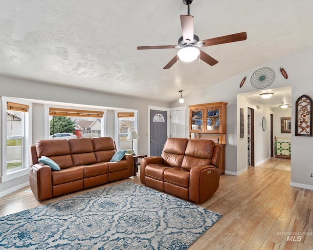 living room with light wood finished floors, baseboards, vaulted ceiling, a textured ceiling, and a ceiling fan