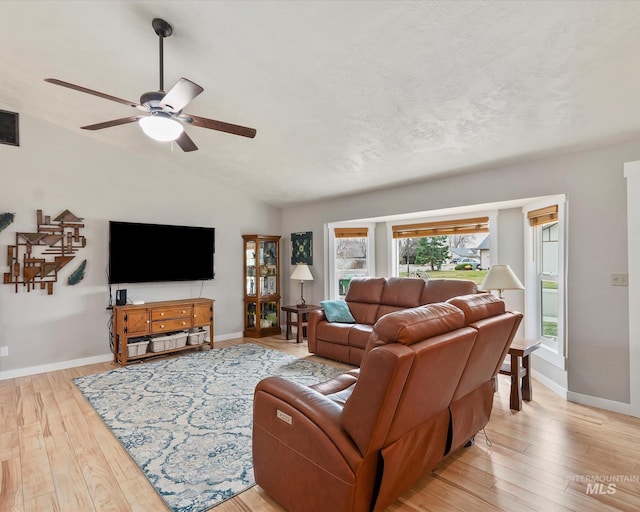 living area with baseboards, light wood finished floors, lofted ceiling, ceiling fan, and a textured ceiling