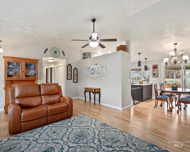 living area featuring ceiling fan with notable chandelier, baseboards, light wood-style floors, and lofted ceiling