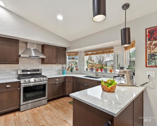 kitchen with stainless steel gas range, lofted ceiling, a sink, decorative backsplash, and wall chimney exhaust hood