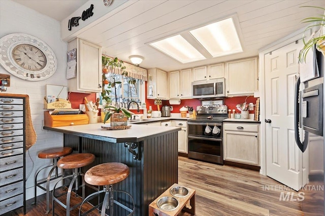 kitchen with a kitchen breakfast bar, kitchen peninsula, sink, hardwood / wood-style flooring, and stainless steel appliances