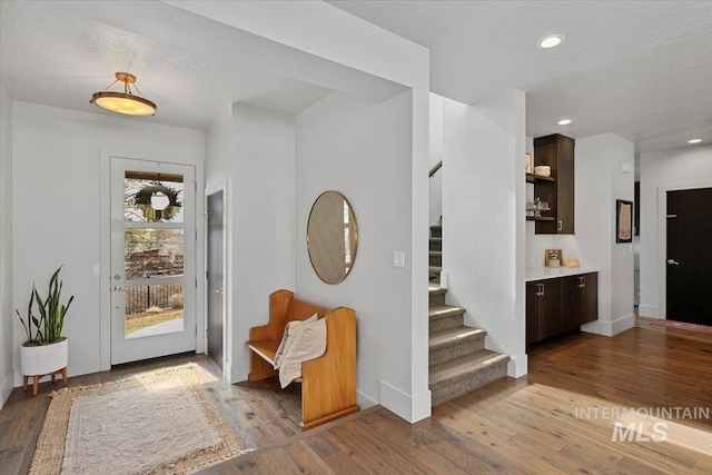 foyer with recessed lighting, a textured ceiling, wood finished floors, and stairs