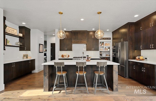 kitchen with open shelves, dark brown cabinetry, stainless steel refrigerator with ice dispenser, and light countertops