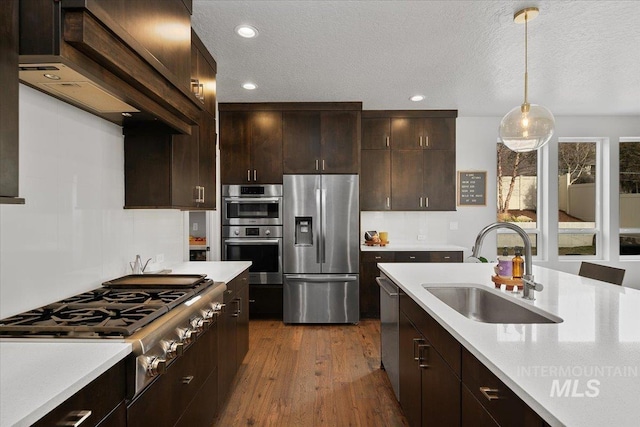 kitchen with a sink, dark wood finished floors, dark brown cabinetry, appliances with stainless steel finishes, and light countertops