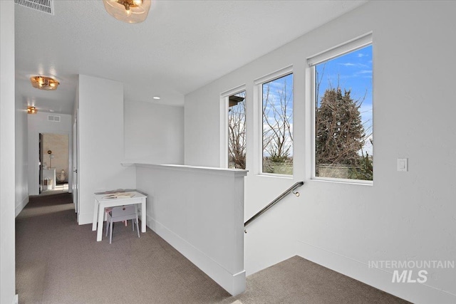 hallway with an upstairs landing, carpet flooring, and visible vents