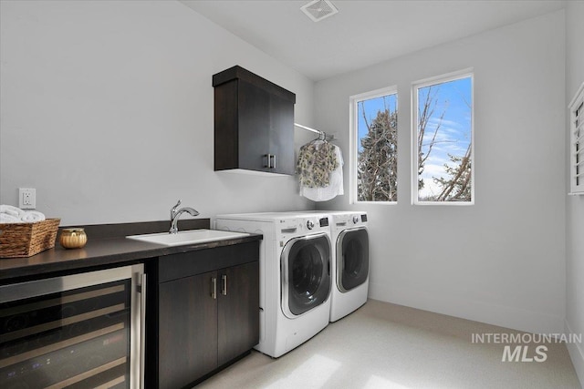 clothes washing area with visible vents, beverage cooler, a sink, cabinet space, and separate washer and dryer