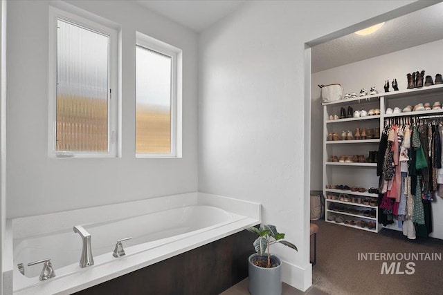 full bath with a garden tub, a spacious closet, and a textured ceiling