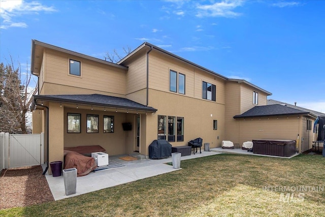 rear view of house featuring a patio, a gate, a yard, and a hot tub