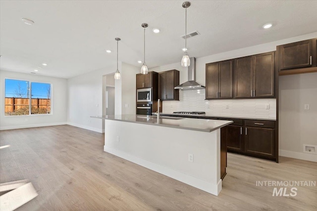 kitchen featuring pendant lighting, an island with sink, wall chimney exhaust hood, and appliances with stainless steel finishes