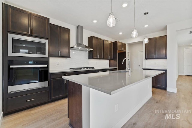 kitchen featuring appliances with stainless steel finishes, pendant lighting, sink, a center island with sink, and wall chimney exhaust hood