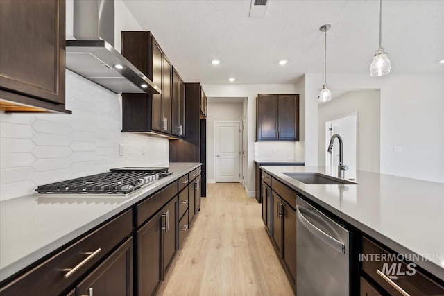 kitchen featuring appliances with stainless steel finishes, sink, hanging light fixtures, dark brown cabinets, and wall chimney exhaust hood